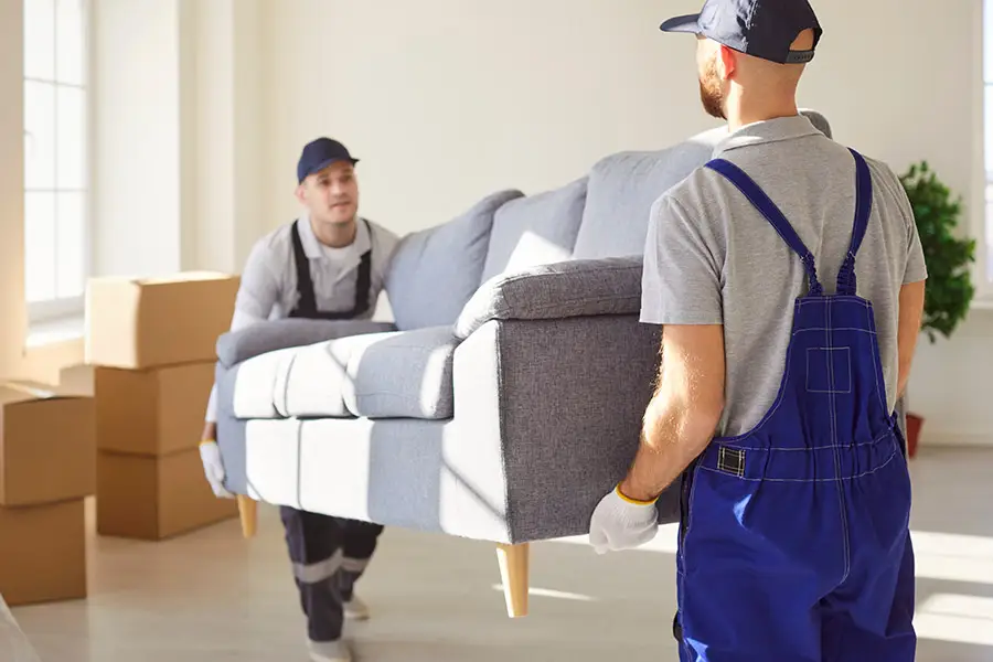 Zwei Möbelpacker tragen eine Couch aus einem Wohnzimmer